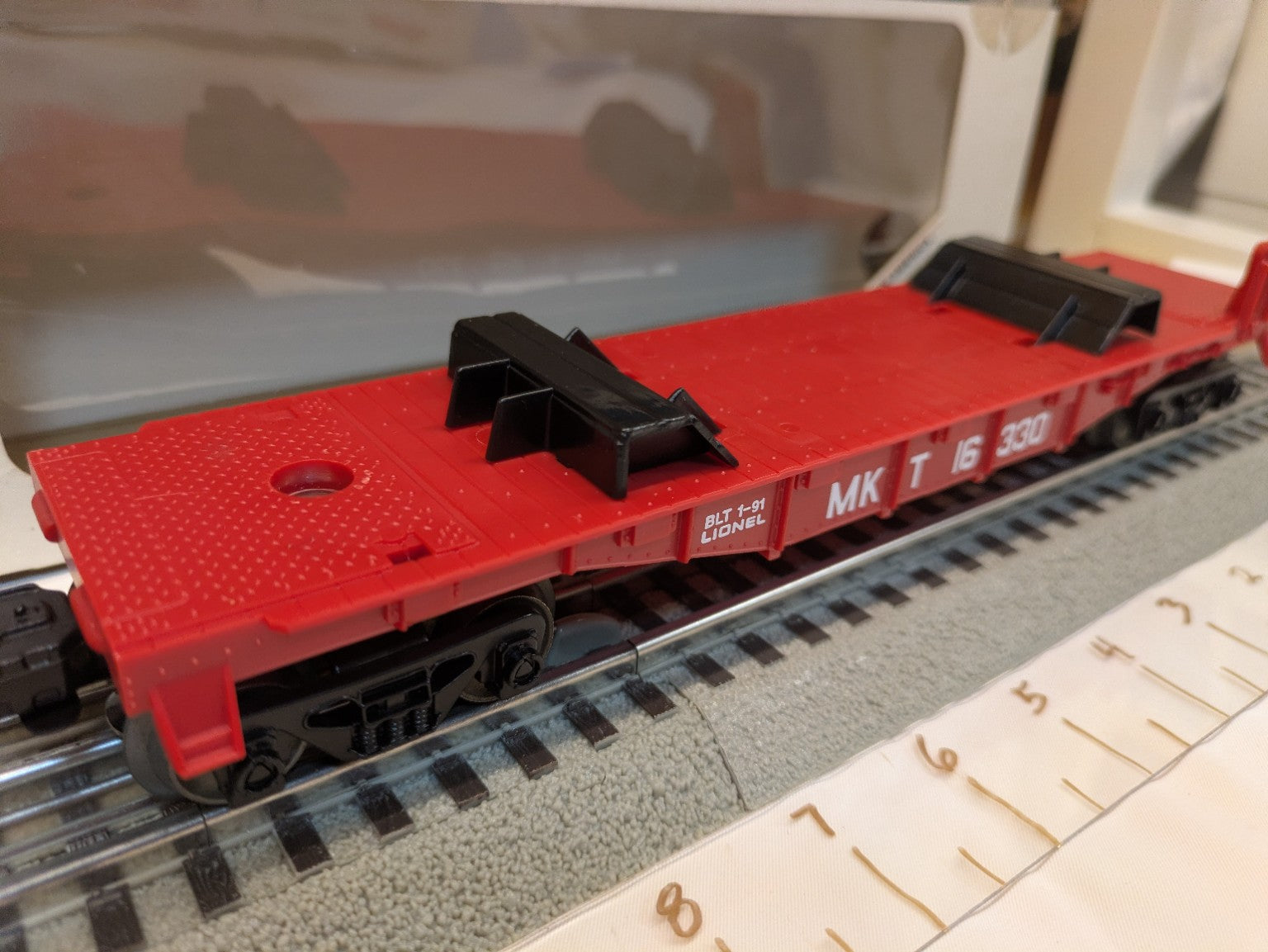 Side view of empty red Lionel 6-16330 Katy flatcar