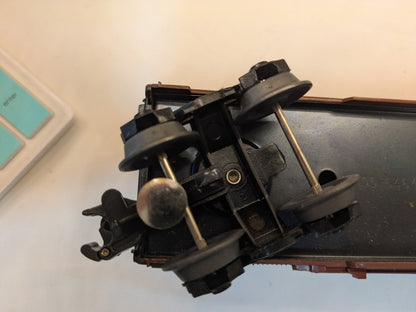 A close-up of a model train's undercarriage and wheels, shown upside down on a dark surface against a light background.
